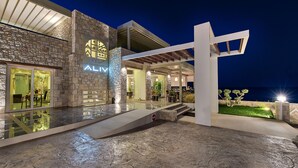 A modern hotel exterior with a stone facade, a covered outdoor area, and a pool. - Aliv Stone Suites & Spa (Zakynthos)
