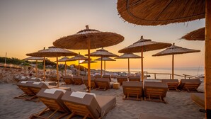 A beachside lounge area with wooden lounge chairs and thatched umbrellas, overlooking the sea. - Aliv Stone Suites & Spa (Zakynthos)