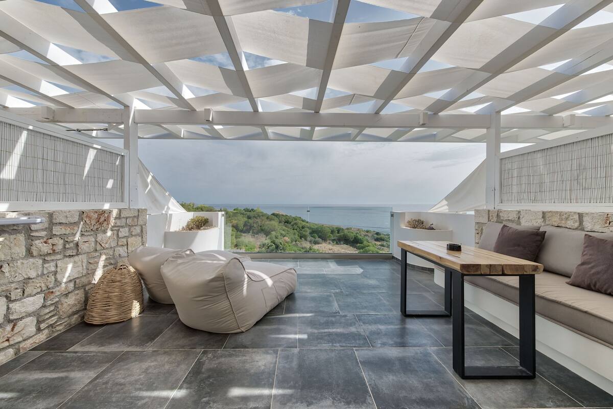 An outdoor patio with a stone wall, a wooden table, a sofa, and a bean bag.