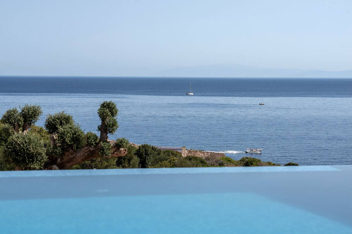 A view of a pool overlooking a calm sea with boats, trees, and a distant shoreline.