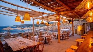 An outdoor dining area with wooden tables and chairs, hanging wicker lamps, and a view of the sea. - Aliv Stone Suites & Spa (Zakynthos)