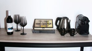 A wooden table with a wine bottle, two wine glasses, a framed tea shop sign, a coffee pot, and a portable espresso maker. - Stalis Drops (Hersonissos)