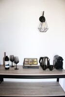 Una mesa de madera con una botella de vino, dos copas de vino, un letrero enmarcado de una tienda de té, una cafetera y una máquina de espresso portátil.