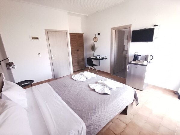 Quarto de hotel com cama, escrivaninha, cadeira, televisão e cozinha compacta.