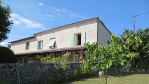 A two-story house with a stone wall in front, a small garden, and a tree. - Individual countryside house in a small village (Cercles)
