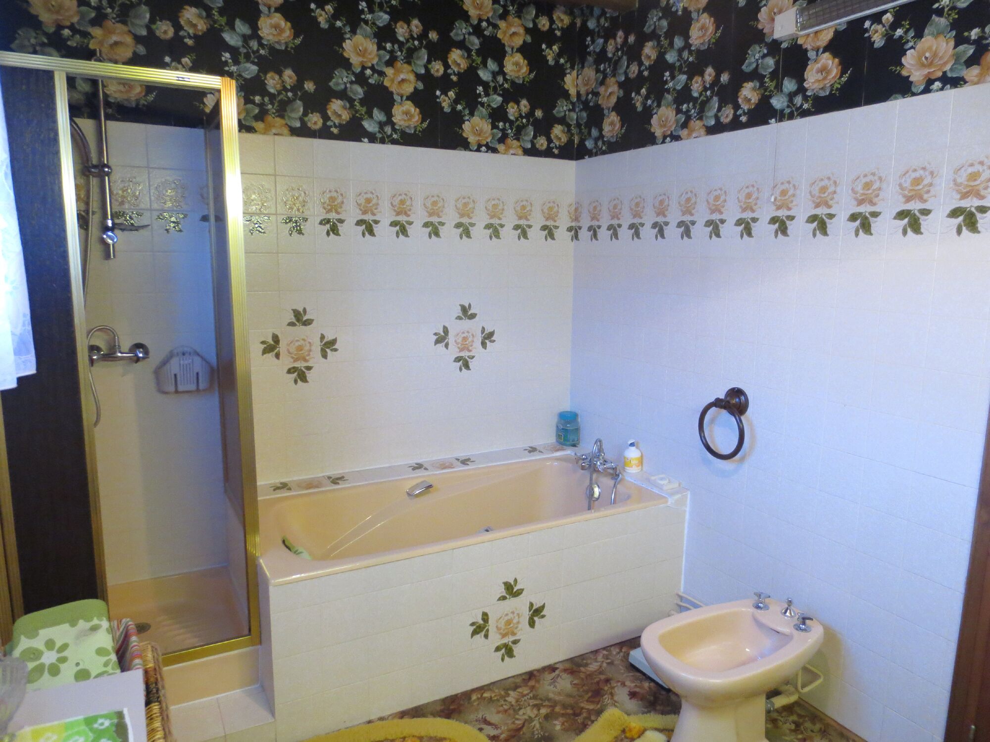 Un baño con bañera, lavamanos e inodoro. Cuenta con zona de ducha con puerta de vidrio. Las paredes están decoradas con azulejos florales.
