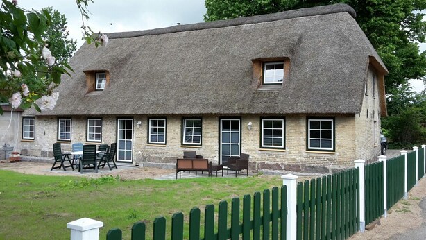 Ett traditionellt hus med halmtak, många fönster och en inhägnad trädgård.