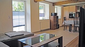 Ett modernt vardagsrum med ett soffbord i glas, en soffa och en matplats med ett bord och stolar.
