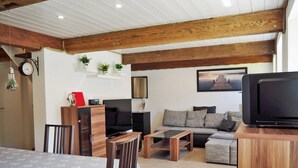 Ett mysigt vardagsrum med ett träpanelat tak, en soffa, en tv och en matplats med ett bord och stolar.