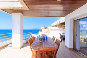 Una mesa de madera con sillas en un balcón exterior con vistas al mar.