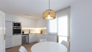 Una cocina moderna con armarios blancos, horno empotrado, lavavajillas y una mesa de comedor redonda con sillas.