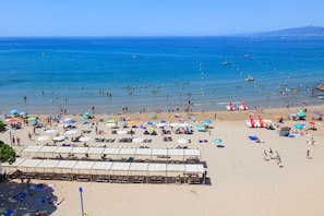 A beach with sun loungers, umbrellas, and a beach hut.