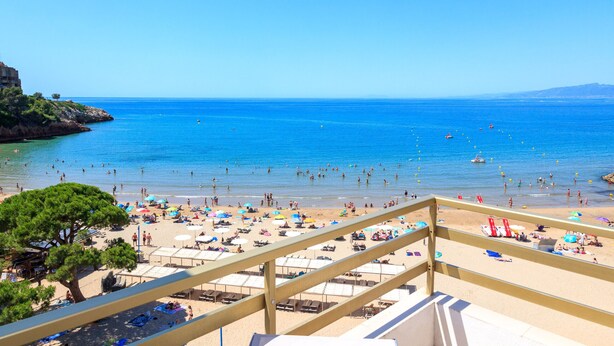 Una playa con barandilla de madera, sombrillas y gente nadando.