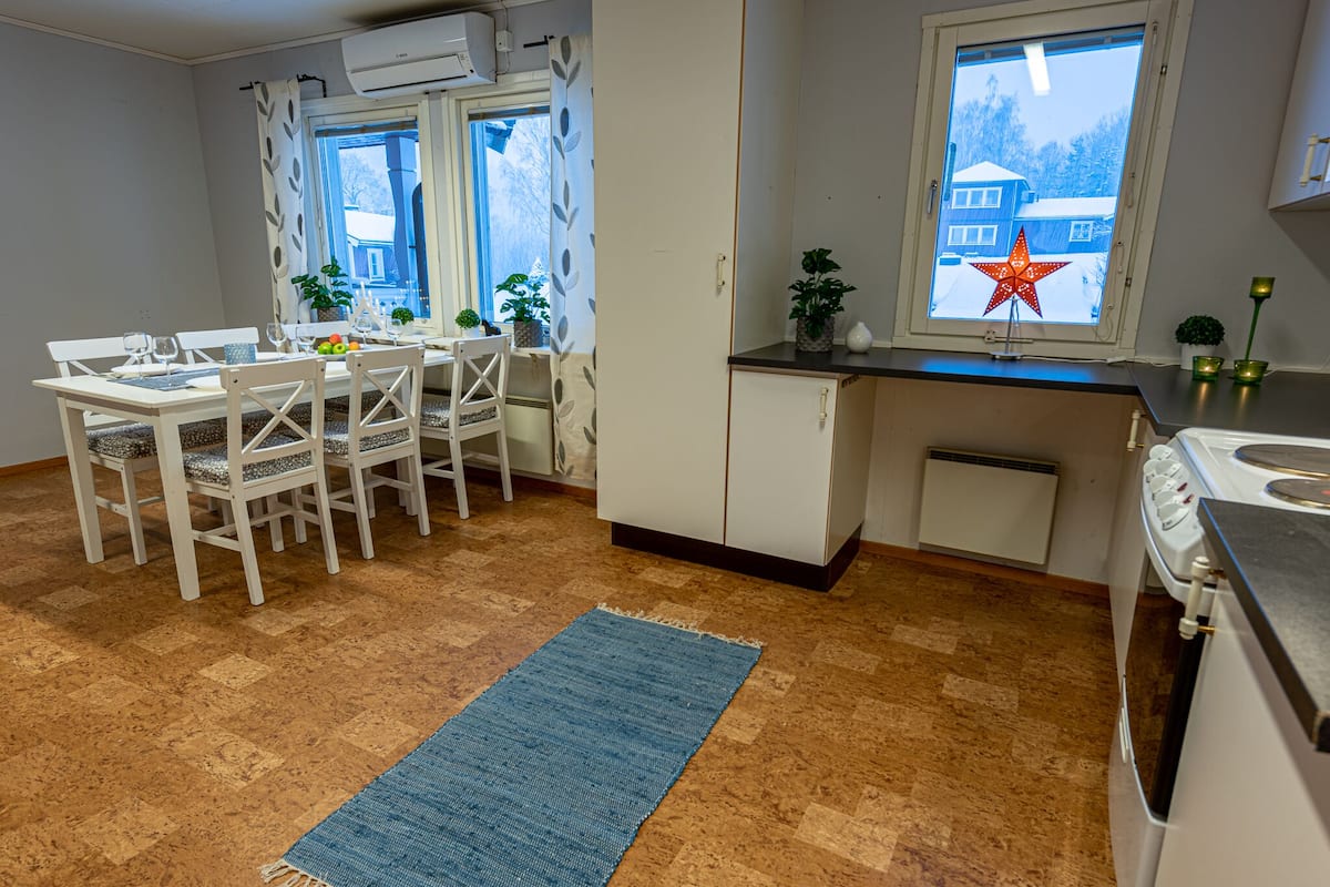 A compact kitchen with a dining area, featuring a window with a star decoration, a white refrigerator, and a stove.