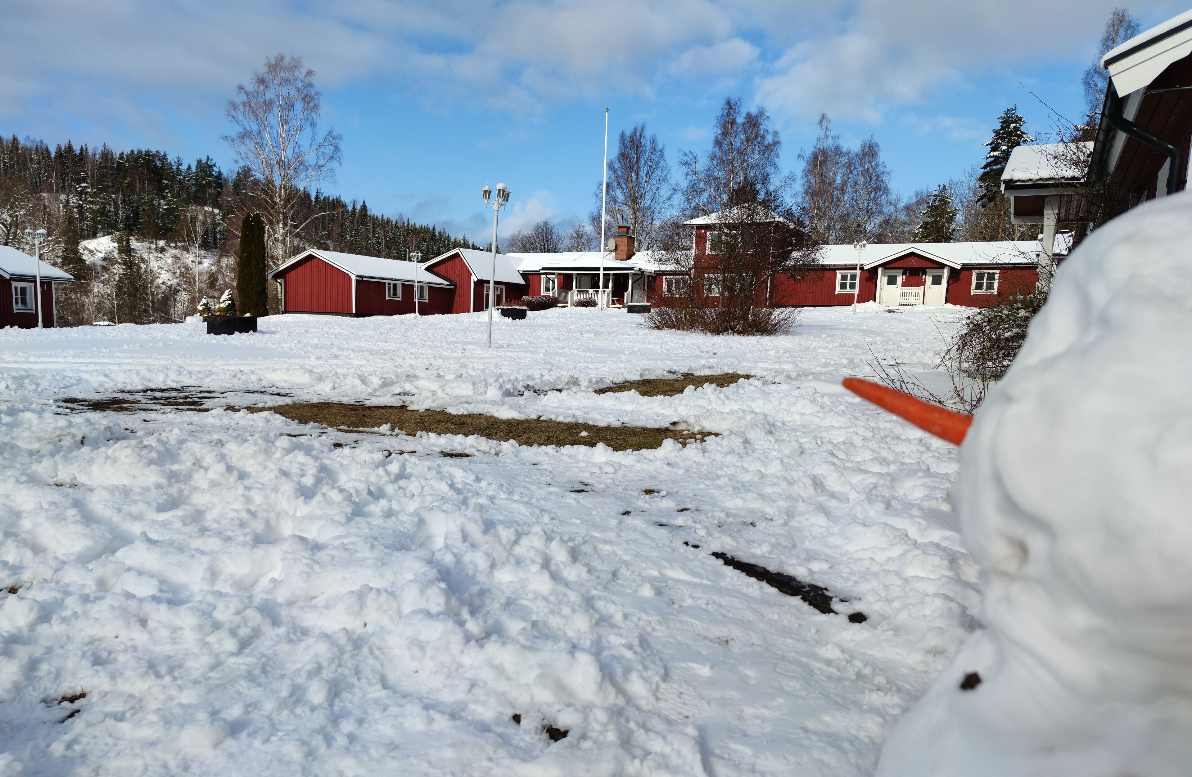 A snow-covered landscape with a row of red buildings, a clear sky, and a small stream.