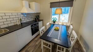 Una cocina compacta con armarios blancos, encimera negra y comedor con mesa negra y sillas blancas.