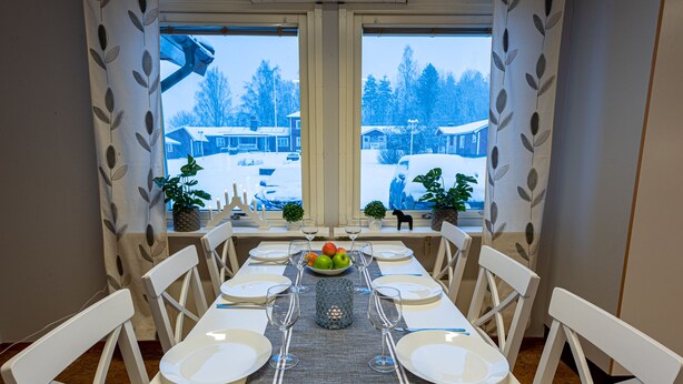 Mesa de comedor preparada para seis personas, con sillas blancas, un frutero y una decoración central.