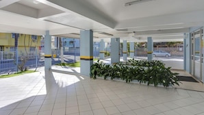 A spacious indoor area with tiled flooring, blue pillars, and a row of green plants. - Marazul Apart Hotel II (Florianopolis)