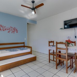 A room with a bed, a dining table with chairs, a ceiling fan, and a television mounted on the wall.