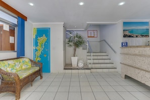 A reception area with a wicker sofa, a blue door, a map, a staircase, and a view of the sea. - Marazul Apart Hotel II (Florianopolis)