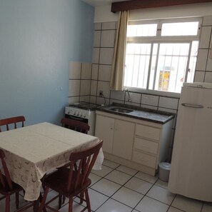 A compact kitchen with a dining table, chairs, a stove, a sink, and a refrigerator.