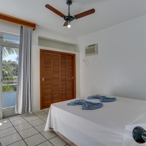 A hotel room with a bed, a ceiling fan, a window with curtains, and a door. - Marazul Apart Hotel II (Florianopolis)