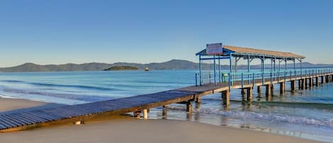 Una playa con un muelle de madera que lleva a una zona cubierta con un letrero.