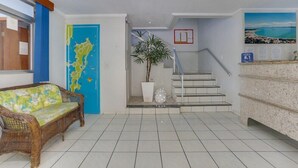 A reception area with a wicker sofa, a blue door with a map, a staircase, and a plant. - Marazul Apart Hotel II (Florianopolis)