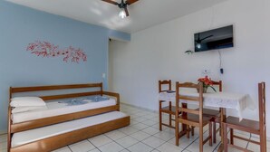 A room with a bed, a desk with chairs, a ceiling fan, and a TV on the wall. - Marazul Apart Hotel II (Florianopolis)