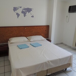 A hotel room with a bed, two pillows, a wooden headboard, a wall map, a telephone, and a tiled floor. - Marazul Apart Hotel II (Florianopolis)