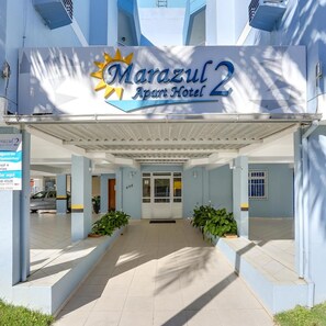 Entrada del Hotel Apartotel Marazul 2, con un paseo techado, plantas en macetas y un cartel que indica las comodidades.