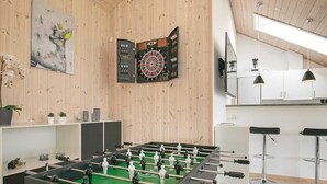 Huoneessa on pöytäjalkapallopeli, seinät ovat puuta, ja siellä on myös dart-taulu ja baarijakkarat.