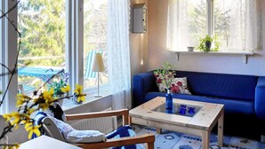 Een gezellige woonkamer met een blauwe bank, een houten salontafel en uitzicht op een tuin door grote ramen.
