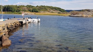 Een steiger met een boot, helder water en een heuvelachtig landschap op de achtergrond.