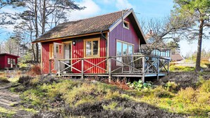 Een rode en paarse hut met een houten terras, omringd door natuurlijke begroeiing.