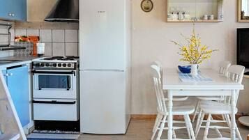 Een keuken met een Bosch koelkast, een fornuis en een eethoek met witte stoelen en een tafel.