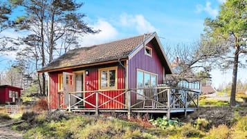 Een rode en paarse blokhut met een houten terras, omringd door natuurlijke begroeiing.