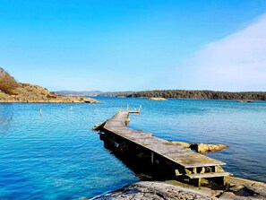 A wooden pier extending into a calm lake with clear blue water, surrounded by rocky terrain and forested hills. - 4 Person Holiday Home in Ellos (Ellos)