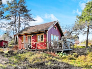 A red and purple wooden house with a porch, surrounded by natural vegetation. - 4 Person Holiday Home in Ellos (Ellos)