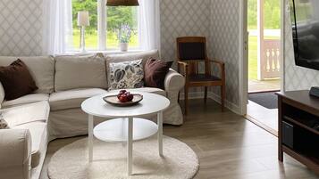 Sala de estar con sofá, una mesita redonda con manzanas, una silla de madera, televisión y un papel tapiz estampado.