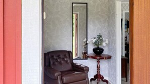Um quarto com uma poltrona de couro marrom, uma mesinha de madeira com um vaso de flores e um espelho grande na parede.