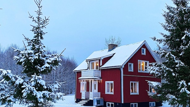 Uma casa vermelha de dois andares com varanda, rodeada por árvores cobertas de neve.