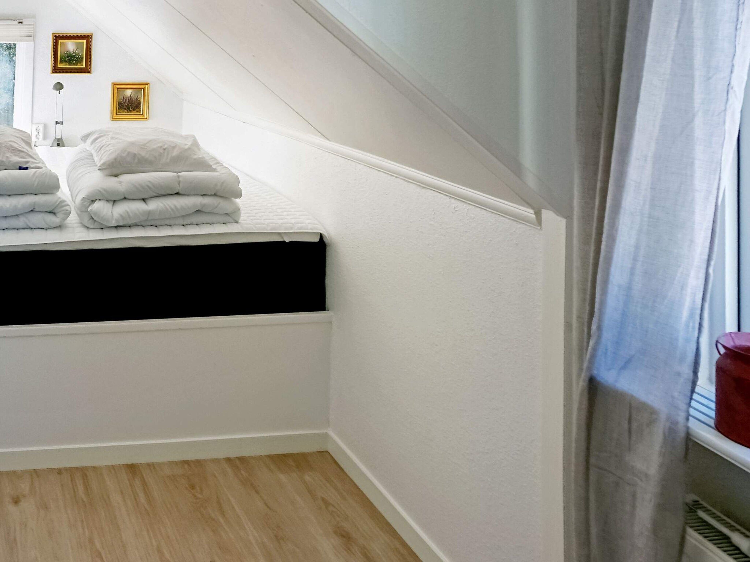 A bedroom with a sloped ceiling, a bed with white bedding, a black mattress, and two framed pictures on the wall.