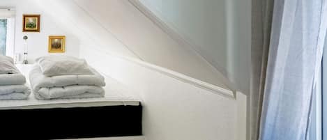 A bedroom with a sloped ceiling, a bed with white bedding, a black mattress, and two framed pictures on the wall.