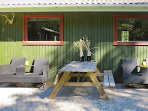 An outdoor seating area with wicker chairs and a wooden table, set against a green wall with two windows. - 4 Person Holiday Home in Hals (Hals)