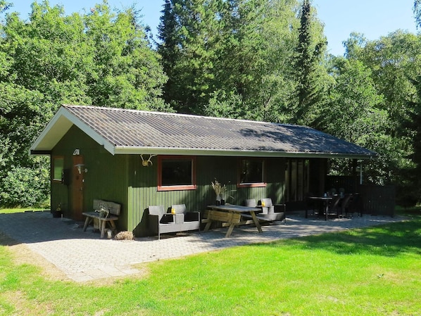 A small, green wooden cabin with a tiled patio, a bench, and a table. - 4 Person Holiday Home in Hals (Hals)