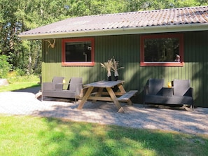 A green building with two windows and a patio area with wicker furniture and a wooden table. - 4 Person Holiday Home in Hals (Hals)