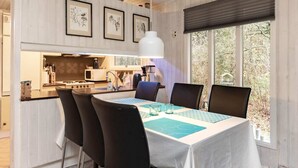 A dining area with a table set for four, a kitchen in the background, and a window with a view of trees. - 4 Person Holiday Home in Hals (Hals)