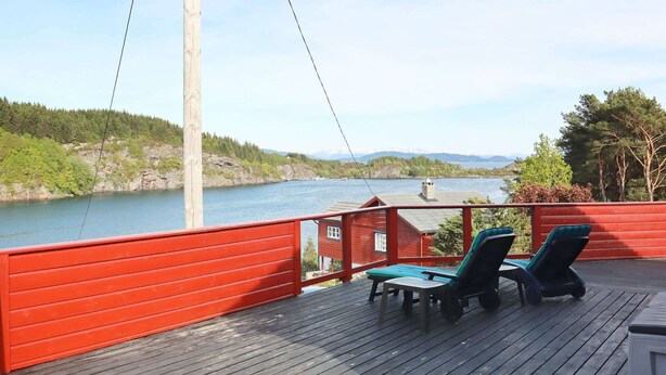 Une terrasse en bois avec deux chaises longues et une table, d’où l’on a vue sur un lac bordé d’une forêt et sur des montagnes au loin.