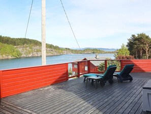 A wooden deck with two lounge chairs and a table, overlooking a lake with a forested shoreline and distant mountains. - 4 Star Holiday Home in Klokkarvik (Oygarden)
